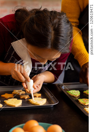 Focused diverse couple in aprons decorating christmas cookies in kitchen Focused diverse couple in aprons decorating christmas cookies in kitchen 120619471