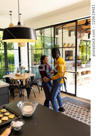 Happy diverse couple in aprons baking christmas cookies, dancing in kitchen, copy space Happy diverse couple in aprons baking christmas cookies, dancing in kitchen, copy space 120619481