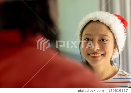 Happy asian woman in christmas hat smiling to diverse partner Happy asian woman in christmas hat smiling to diverse partner 120619517