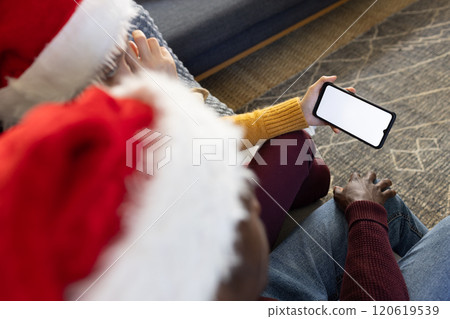 Diverse couple in christmas hats having smartphone video call, copy space screen Diverse couple in christmas hats having smartphone video call, copy space screen 120619539