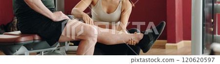 Assisting with Leg Exercise in Fitness Center 120620597