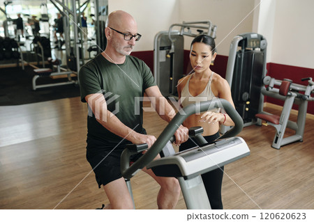 Exercising on Treadmill with Personal Trainer in Gym 120620623