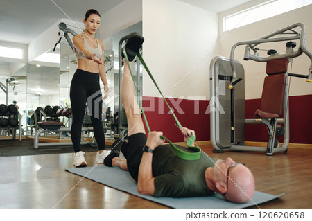 Assisting in Stretching Exercise with Resistance Band at Gym Assisting in Stretching Exercise with Resistance Band at Gym 120620658