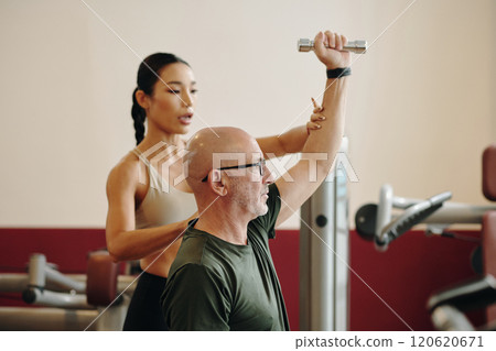 Assisting Senior Man With Strength Training Equipment 120620671