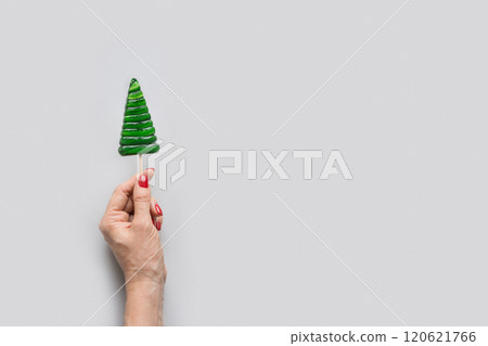 Christmas tree shaped green lollipop in woman hand. Xmas creative minimal greeting card. View from above. Copy space Christmas tree shaped green lollipop in woman hand. Xmas creative minimal greeting card. View from above. Copy space 120621766
