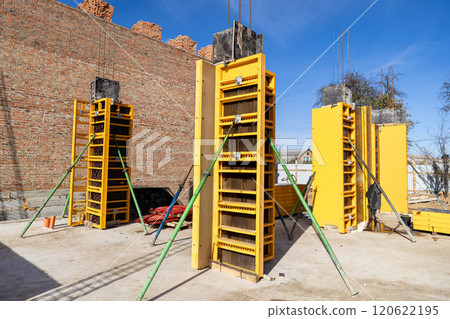 Construction site with yellow column formwork and brick wall, ready for concrete pouring 120622195
