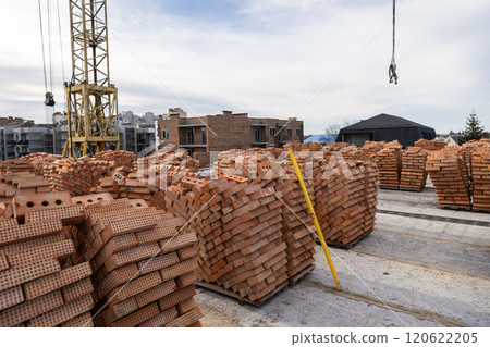 Stacks of red bricks at a construction site with a crane and unfinished buildings in the background Stacks of red bricks at a construction site with a crane and unfinished buildings in the background 120622205