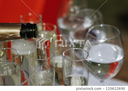 A bottle of champagne is poured into a row of wine glasses 120622690