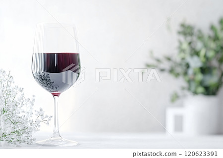 Glass of red wine with white flowers and green plant on white table 120623391