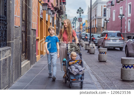 Mother tourist with her toddler and teenage sons walking through the colorful colonial streets of Puebla, Mexico. Travel, cultural exploration, and vibrant architecture concept Mother tourist with her toddler and teenage sons walking through the colorful colonial streets of Puebla, Mexico. Travel, cultural exploration, and vibrant architecture concept 120623536