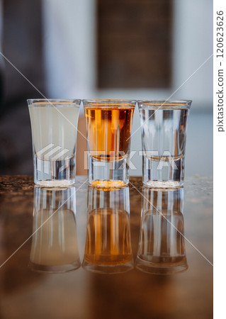 Three glasses of diverse drinks reflecting on a shiny surface for a modern beverage concept 120623626