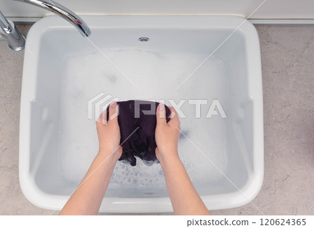 Handwashing violet clothes in a sink filled with soapy water, highlighting a simple and effective laundry routine. 120624365