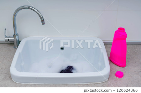 A simple handwashing setup with a pink detergent bottle and soapy water in a sink, highlighting everyday household care. 120624366