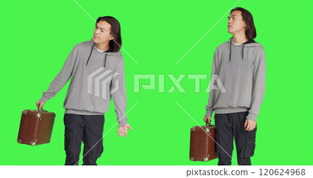 Male model waiting in studio, looking around and checking time on wristwatch. Person carrying vintage suitcase standing over greenscreen backdrop, acting impatient on camera. Male model waiting in studio, looking around and checking time on wristwatch. Person carrying vintage suitcase standing over greenscreen backdrop, acting impatient on camera. 120624968