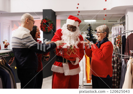 Santa drawing winners names in mall store, presenting lucky prize owners extracted from red raffle contest box. African american adult in festive outfit greeting diverse clients at shopping center. Santa drawing winners names in mall store, presenting lucky prize owners extracted from red raffle contest box. African american adult in festive outfit greeting diverse clients at shopping center. 120625043