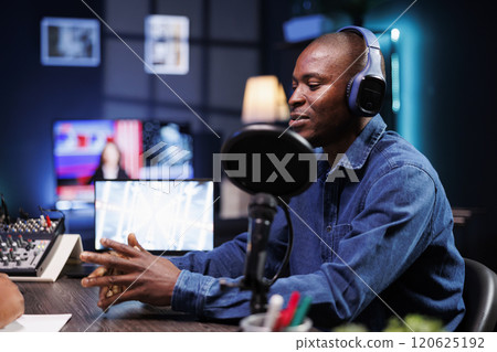Male radio host having a chat with someone while recording using audio equipment so that listeners can hear it live. Influencer having a conversation and airing a discussion with journalist. 120625192