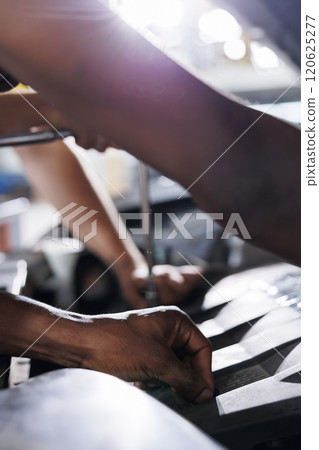 Mechanics team in car service using professional mechanical tool to repair broken engine. Hardworking workers in garage repairing client automobile, ensuring optimal automotive performance, close up 120625277