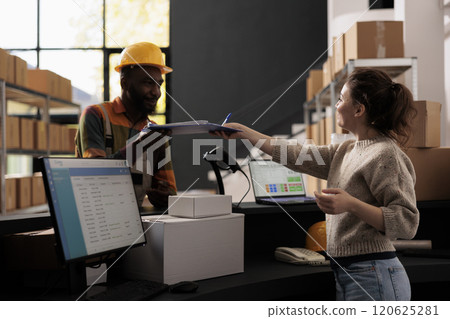 African american employee showing papers with clients orders to warehouse supervisor, dicussing shipping details before start preparing packages. Diverse stockroom team working in storehouse African american employee showing papers with clients orders to warehouse supervisor, dicussing shipping details before start preparing packages. Diverse stockroom team working in storehouse 120625281