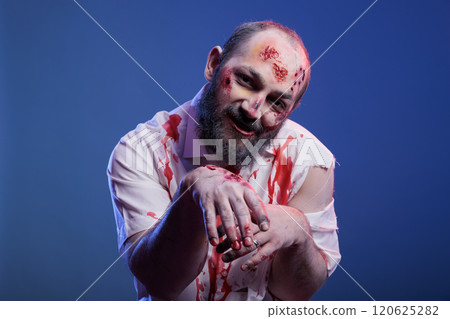 Portrait of devilish possessed zombie with blood on face and clothes isolated over studio background. Spooky reanimated corpse ghoul growling creepily, starving for human brains Portrait of devilish possessed zombie with blood on face and clothes isolated over studio background. Spooky reanimated corpse ghoul growling creepily, starving for human brains 120625282