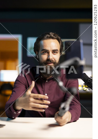 Expressive man using smartphone on selfie stick to shoot video, doing frantic gesturing. Animated influencer making hectic hand movements while filming vlog with phone in studio 120625293