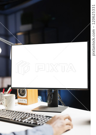 Freelance employee sitting at home using blank desktop screen, staring at white template on computer display. At his desk, african american contractor studies an isolated empty monitor. Freelance employee sitting at home using blank desktop screen, staring at white template on computer display. At his desk, african american contractor studies an isolated empty monitor. 120625331