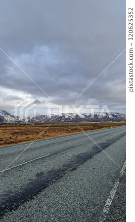 Icelandic scenery with lonely road in nordic setting with wintry weather, empty frozen roadside and pastures near snowy mountain chain. Fantastic view of countryside in iceland. Icelandic scenery with lonely road in nordic setting with wintry weather, empty frozen roadside and pastures near snowy mountain chain. Fantastic view of countryside in iceland. 120625352