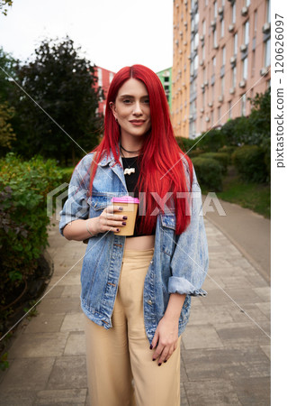 Young woman with vibrant red hair enjoying a drink in an urban setting 120626097