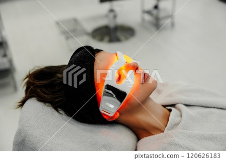 Woman receiving facial treatment with LED technology in spa setting 120626183