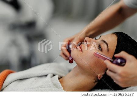 Woman receiving a facial treatment with a roller tool in a spa setting Woman receiving a facial treatment with a roller tool in a spa setting 120626187