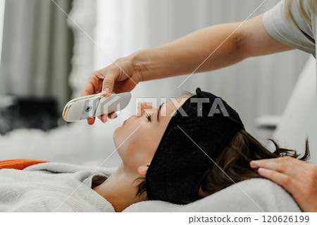 Woman receiving facial treatment at spa with handheld device for skin care 120626199