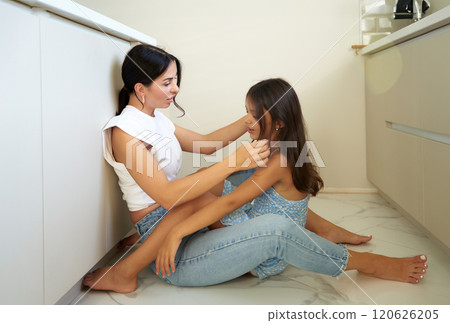 Mother and daughter bonding while sitting on a kitchen floor in a cozy home in sunlight Mother and daughter bonding while sitting on a kitchen floor in a cozy home in sunlight 120626205