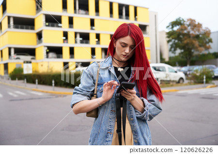 Young woman with red hair checks phone while walking through parking lot Young woman with red hair checks phone while walking through parking lot 120626226