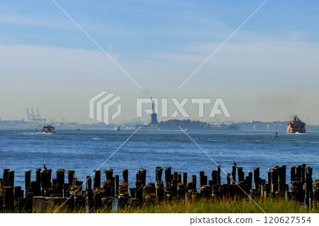 Clear day reveals Statue of Liberty distance, surrounded by boats navigating harbor wooden pilings emerge from water in tranquil scene at NYC New York Clear day reveals Statue of Liberty distance, surrounded by boats navigating harbor wooden pilings emerge from water in tranquil scene at NYC New York 120627554