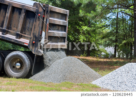 Truck unloads gravel onto grassy area preparing for landscaping work process demonstrates delivery of construction materials for improvement projects. Truck unloads gravel onto grassy area preparing for landscaping work process demonstrates delivery of construction materials for improvement projects. 120628445