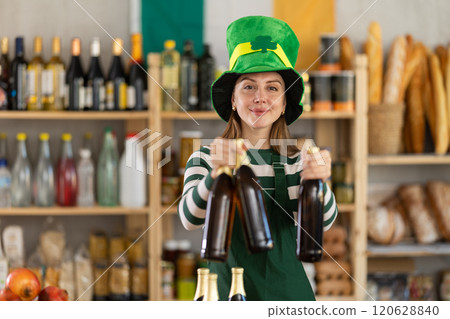 Positive friendly girl seller in traditional green Irish cap offers to buy Irish ale for St. Patrick Day celebration 120628840