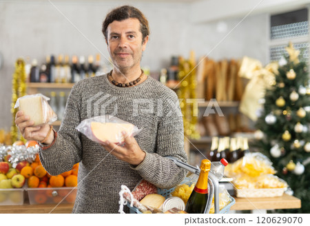 Positive adult man with shopping cart picking out fresh cheese to buy in grocery store for christmas table Positive adult man with shopping cart picking out fresh cheese to buy in grocery store for christmas table 120629070