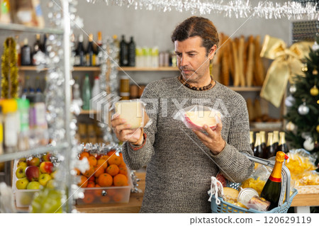 Man choosing cheese in grocery store adorned with Christmas ornaments 120629119