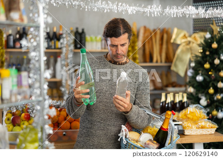 Portrait of focused glad positive man purchasing bottled water in grocery store for christmas table Portrait of focused glad positive man purchasing bottled water in grocery store for christmas table 120629140