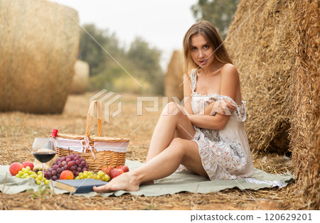 Pretty woman in white dress sitting near haystack on picnic 120629201