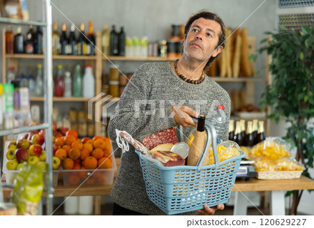 Adult male customer with shopping cart choosing products, looking for something in supermarket 120629227