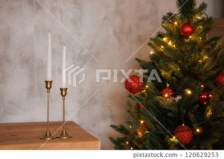 A Christmas tree with red balls and a pair of candles on a table 120629253
