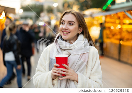 Young woman stands with glass of hot coffee in her hands and enjoys festive New Year atmosphere 120629328