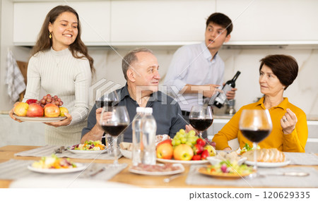 Father and mother together with adult children talking at dinner table at home 120629335