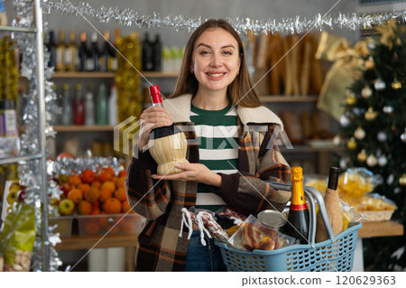 Female shopper with grocery cart chooses wine for celebrating Christmas or New Year 120629363