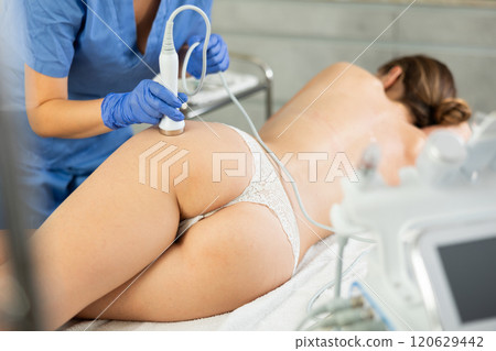Professional cosmetician performing hardware body treatment, electric massage and moisturizing bottom layer of skin for young woman in clinic of esthetic cosmetology Professional cosmetician performing hardware body treatment, electric massage and moisturizing bottom layer of skin for young woman in clinic of esthetic cosmetology 120629442