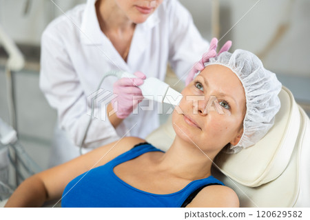 Young female cosmetologist doing exfoliating procedure to adult woman Young female cosmetologist doing exfoliating procedure to adult woman 120629582