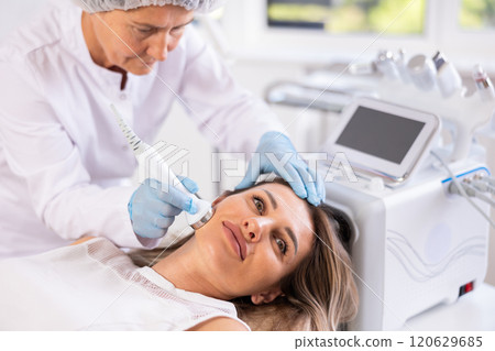 Young female patient receiving high frequency ultrasonic facial procedure 120629685