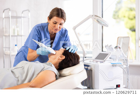 Female cosmetologist performing facial skin cleansing with ultrasonic shovel on woman 120629711