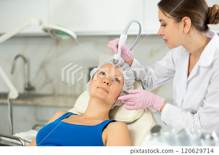 Happy adult woman getting facial deep hydration procedure from experienced cosmetologist in medicine office. Concept of professional cosmetology and rejuvenation 120629714