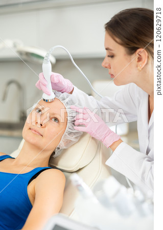 Young woman cosmetologist doing ultrasound procedure to adult woman Young woman cosmetologist doing ultrasound procedure to adult woman 120629718